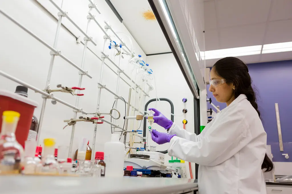 Chimiste en blouse, lunettes et gants nitrile sous une hotte